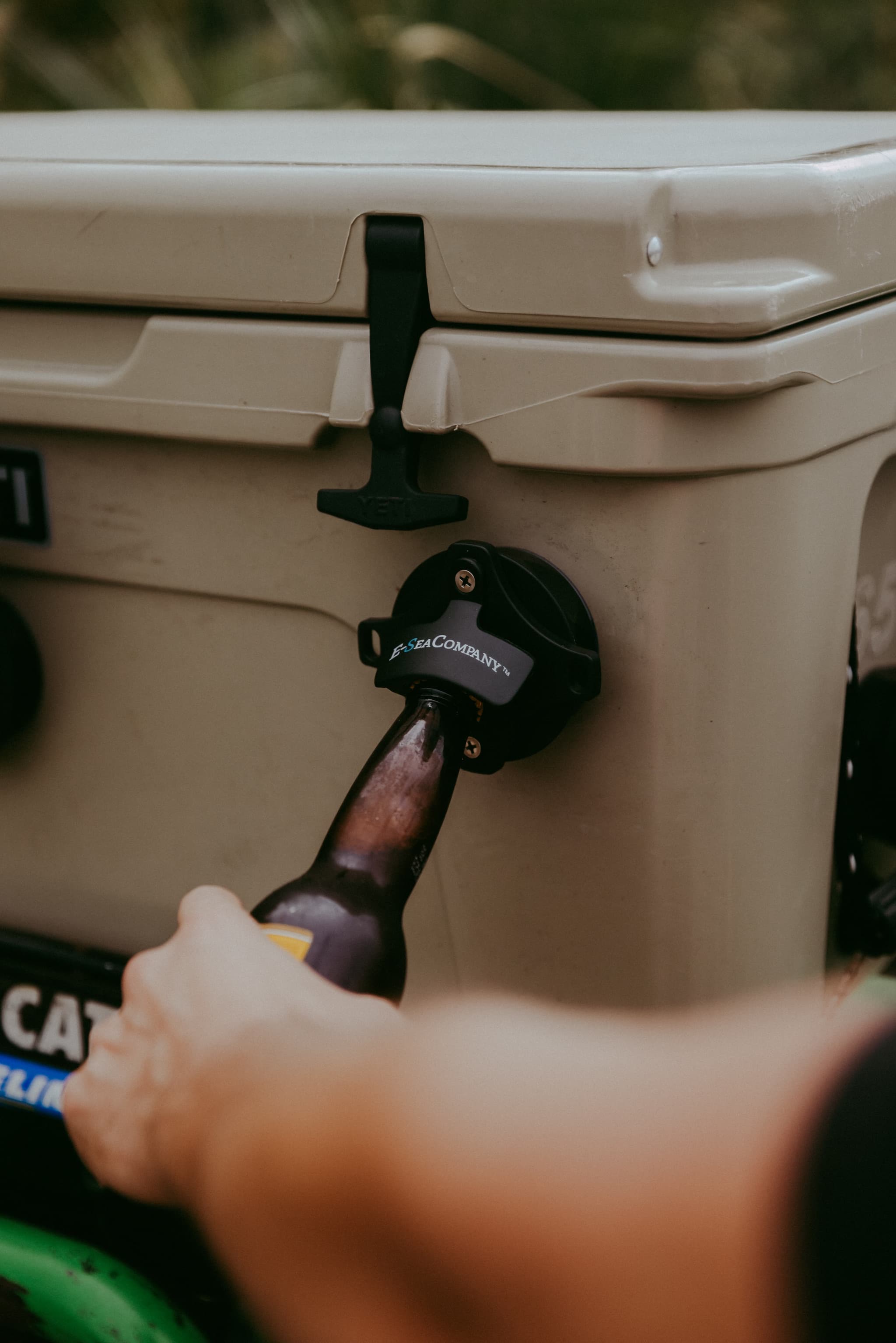 A cold beer being opened with an E-Sea Bottle Opener suction mounted to a tan Yeti Cooler 