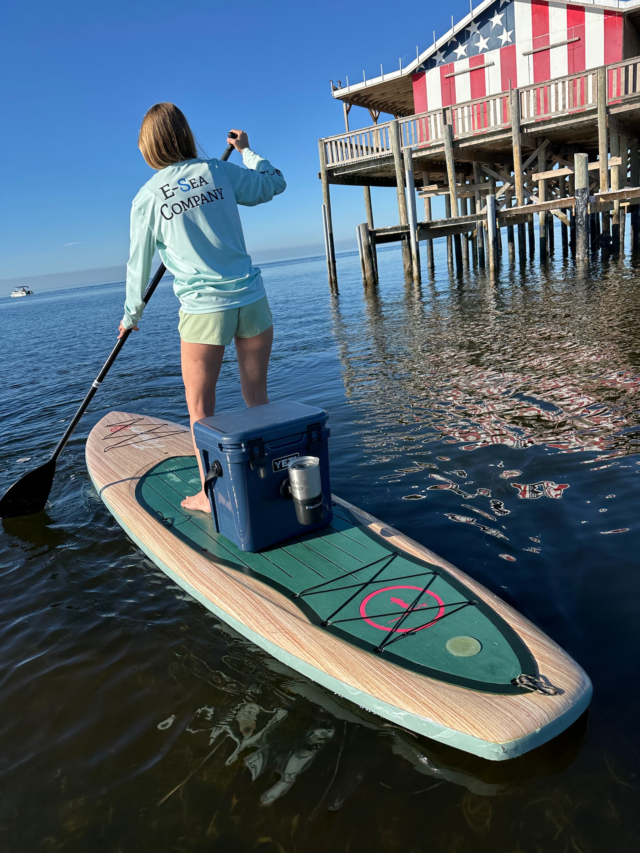 Yolo paddle board with a Yeti cooler secured on the board and a E-Sea Cup Adjusatable suction mounted to the cooler against a patriotic stilt home