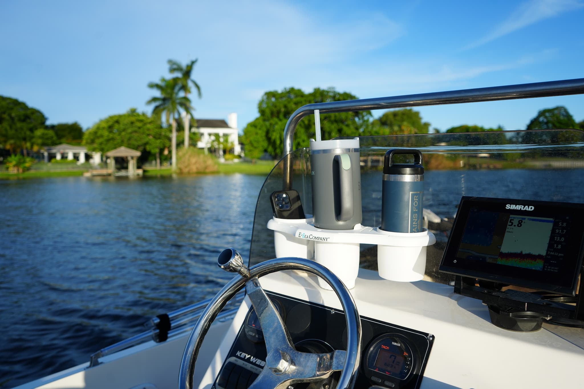 Boat's steering wheel and dashboard with a scenic background of water and the E-Sea Caddy Cup Holder on boat console next to Simrad