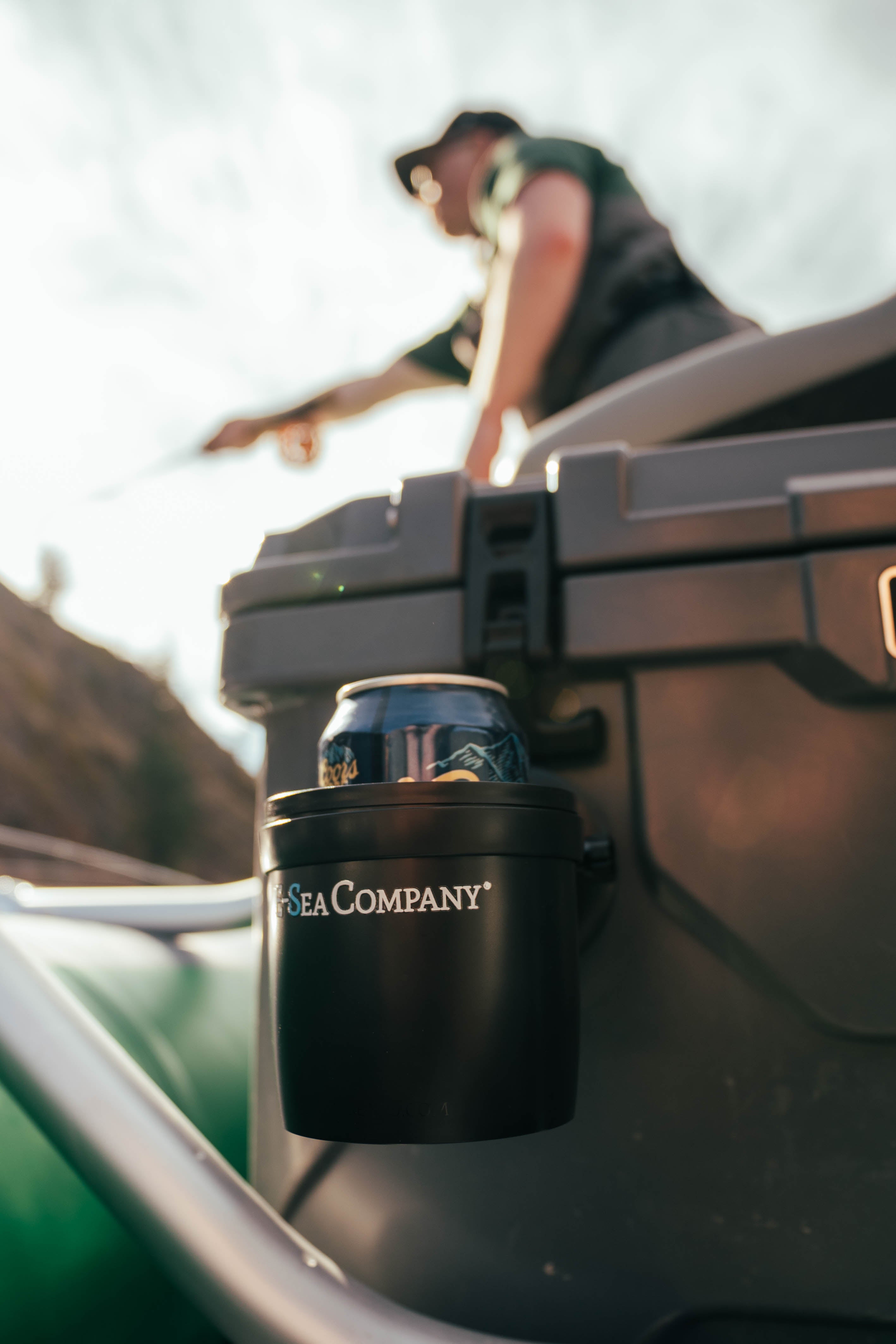 E-Sea cup adjustable drink holder suction mounted to a brown cooler on top of a fishing raft with fly fisherman in the background